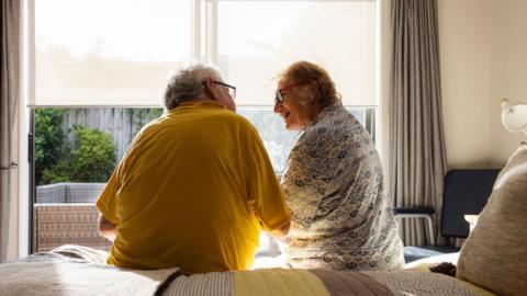 Stock photo of two older people sitting on a bed talking