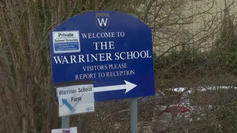 A blue and white sign for the entrance to The Warriner School.
