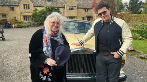 Dwina and RJ in front of a yellow Rolls Royce. It is in front of Robin Gibb's large house, which has a blue plaque.