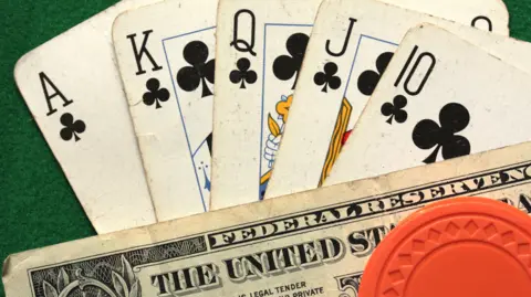 BBC A royal flush in poker - that includes an ace, king, queen, jack and 10 of clubs - are fanned out on a green poker table with a $1 bill and orange chip.
