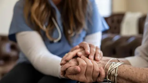 A nurse holds the hands of an elderly woman with lots of bracelets around her arm