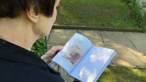 A shot over the shoulder of a woman holding open a book.