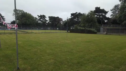 Andy Campbell A green field with some English flags on a pole. Some fencing can be seen in the background. 