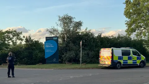 A police officer and police van on the road near a sign saying Severn trent Draycote Water.
