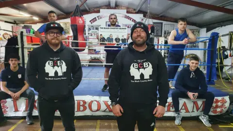 Handout Lee Cadman (left) and Kevin Dillon (right) with a boxing ring behind them and people using it in the gym.