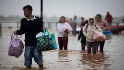 People walk through floodwater carrying their belongings in bags