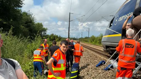James Grierson Several men in high-vis clothing are seen helping passengers off the train