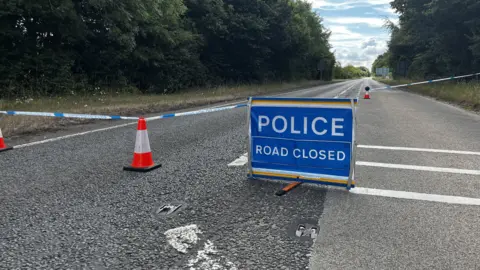 The road closure on the A40. Police tape is across the carriageway with a blue sign in the road. The sign reads 'Police Road Closed' in white lettering.