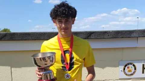 Luis Gabriel Guembes holding a football trophy and wearing yellow football shirt.