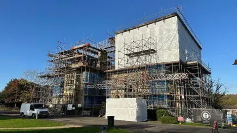 A building covered in scaffolding. There are clear blue skies above.