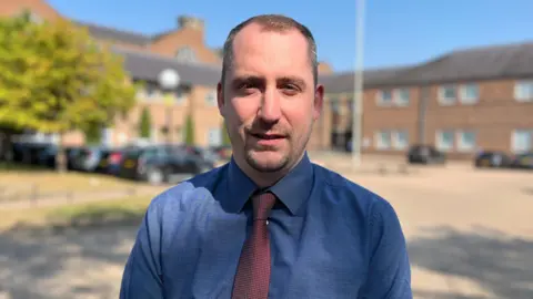 Qays Najm/BBC Detective Sergeant Ricki Peake wearing a blue shirt and red tie outside Norwich Crown Court