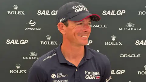 Dylan Fletcher, wearing a GBR cap and t-shirt and stood in front of an advertising board