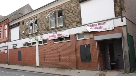 Lancashire Fire and Rescue Service A street, showing a red brick building with stone on the second floor. Signs say function room available. Windows are open on the second floor. On the ground floor, a door is wedged open.