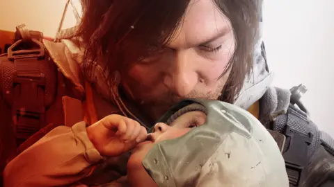 Sony/Kojima Productions Screenshot from Death Stranding 2 shows Norman Reedus' character gently kissing the forehead of a small child, who looks up at him lovingly. The image is almost photorealistic.