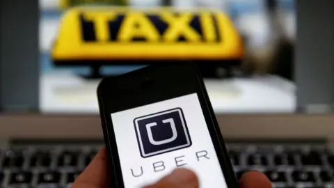 A phone displays shows the word "Uber" in front of a laptop keyboard and screen with the word "taxi" written in bright yellow.