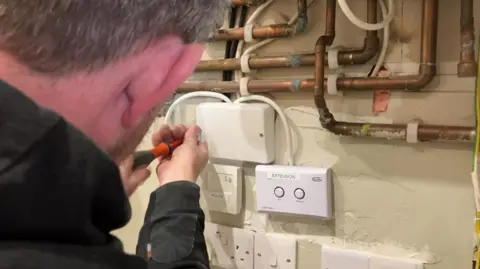 The back view of a close-up of an electrician working on white sockets.