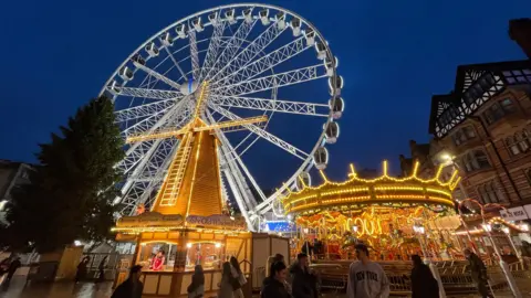 A large observation wheel and carousel at the festive market lit up at night time