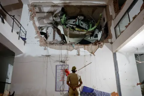 Reuters An official looks up with his arms behind his back and back turned to the camera, as they inspect a huge hole in the wall of a building interior, with some of the plane visible in the hole, on Thursday.