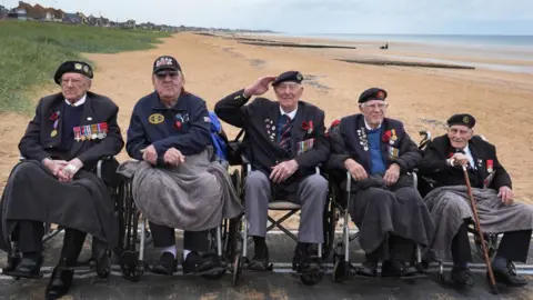 PA Media Five men in wheelchairs on Sword Beach in Normandy. They are wearing veteran uniforms.