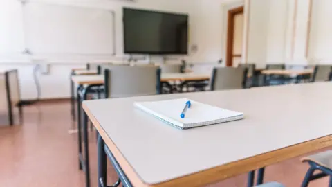 A generic picture of a classroom, with a notepad and pen on a desk in the forefront of the picture.