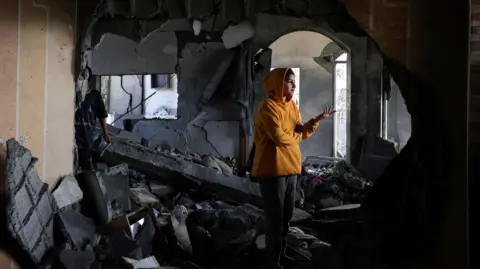 Reuters Reem al-Zanaty, 13, stands on rubble in the remains of her family home in the city of Khan Younis, southern Gaza, following an Israeli air strike (15 May 2025)