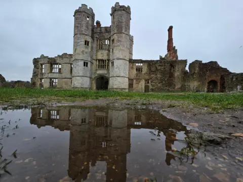 Yen Milne The rear of Titchfield Abbey, a large partly ruined building, with a puddle in the foreground showing its inverted reflection