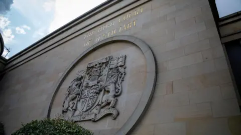 An exterior sandstone wall of the High Court in Glasgow with a crest.