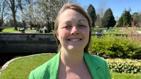 Nicki Scott, Green Party candidate in the Warwickshire County Council election stands facing the camera. She is wearing a green jacket.