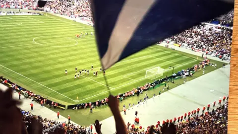 Kevyn Whitelaw Una vista del campo del partido Brasil-Escocia en el Stade De France desde el asiento de Kevyn Whitelaw. Podemos ver al equipo de Escocia frente a la portería, un aficionado ondeando una bandera de Escocia en la mitad superior de la imagen.
