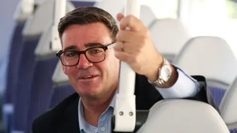 Toby Melville/PA Wire Prime Minister Andy Burnham is pictured during a bus ride during a visit to Bath, Somerset to highlight what the government is doing to help families with the cost of living. He is wearing a black suit jacket and a blue shirt.
