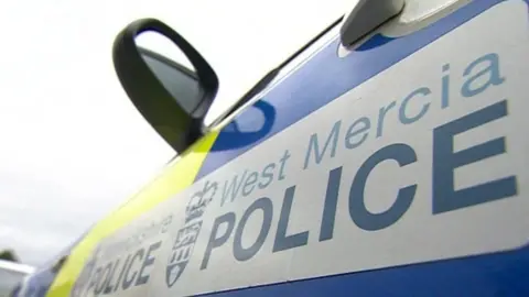 The side of a West Mercia Police vehicle. The car is blue and yellow and branded with the force's name and crest.