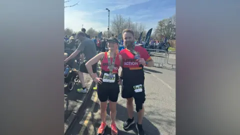 Barry Ahearn Barry Ahearn with Saskia Wickins at the Surrey Half Marathon. Barry and Saskia are both wearing 'Epilepsy Action' gear; Barry a t-shirt and Saskia a vest. Saskia is wearing her medal while Barry is holding his. Both are wearing black shorts and trainers. 