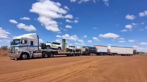 Terry Snell A triple road train on red sandy earth with blue skies and clouds in the background