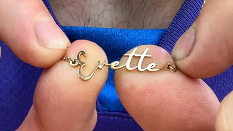 MATT DEAN/BBC A picture of a gold-coloured necklace featuring the name "Evette" is being held up to the camera.