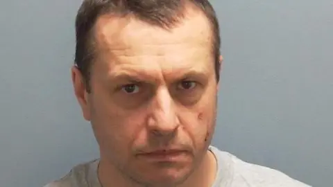 A custody photo of a man with brown hair and wearing a grey jumper