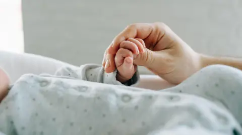An adult hand holding a baby's hand