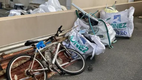 BBC Fly-tipped bags filled with rubbish and a rusty bicycle outside the Amalgamated Boxing Club. 