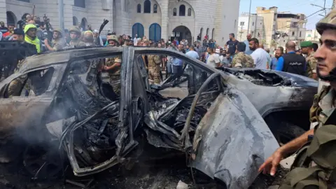 Reuters Mensen staan ​​bij een brandende auto na een Israëlische aanval op een buitenwijk van de Zuid-Libanese stad Sidon (21 augustus 2024)