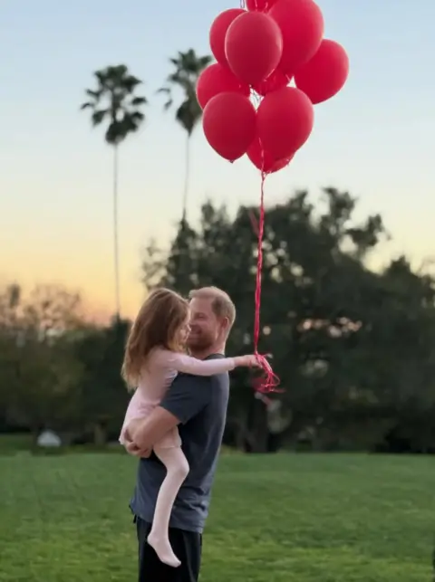 Instagram/Meghan Harry carga a Lilibet, quien sostiene globos rojos.