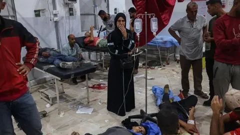 A Palestinian woman looks on as people reportedly injured by Israeli fire while waiting for aid in central Gaza receive care at al-Awda hospital, in Nuseirat refugee camp (24 June 2025)