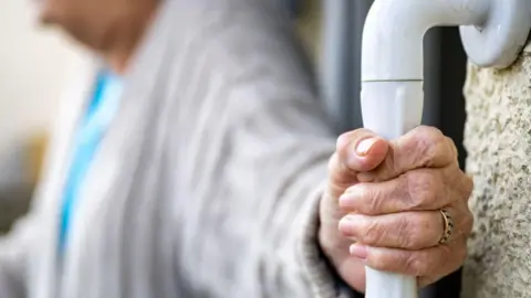 A close-up stock photo of an elderly woman's hand gripping a support bar.