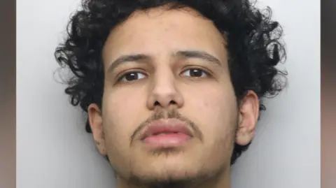 Police custody image of a man with dark curly hair and thin beard.