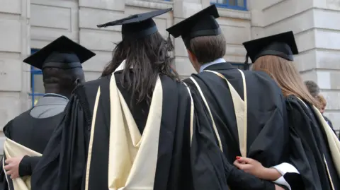 Four students dressed in graduation robes and mortarboards stand with their backs to the camera. 