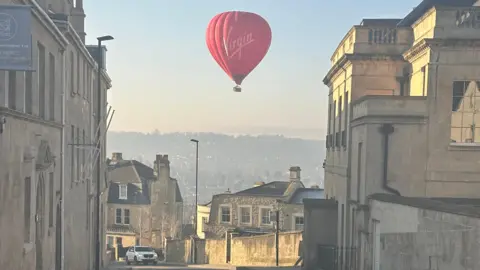 Weather Watcher/Starswood A red hot hair ballon is flying over Charlcombe on a sunny morning. The viewer can see across to Bath over the hill.