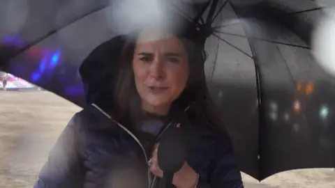 BBC reporter under an umbrella.