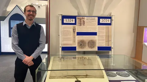 West Norfolk Council Luke Shackell with short brown hair standing next to glass case containing charter