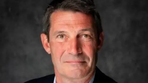 West Midlands Fire Service Close-up of Oliver Lee's face, he is looking at the camera and is in front of a grey background