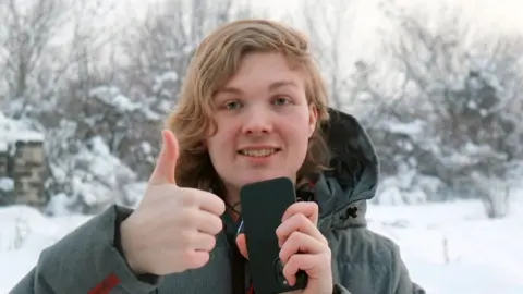 Ada staat buiten in de sneeuw met een warme jas en een mobiele telefoon