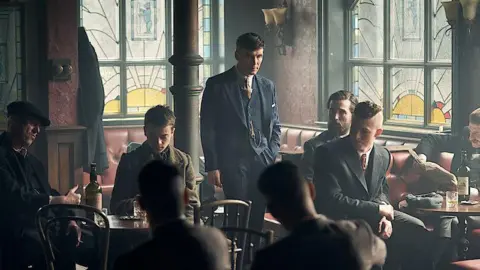 Tommy Shelby, dressed in a 20's style suit, stood in The Garrison pub on the show Peaky Blinders 