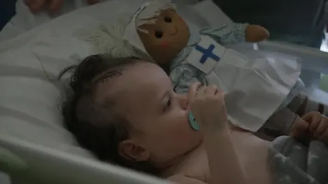 Sienna-Rose in a hospital bed, she has a surgical wound on her head.